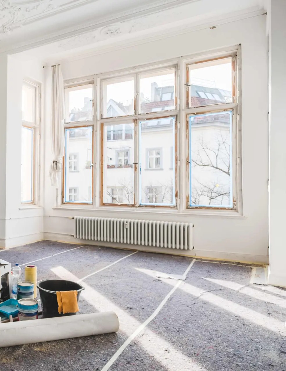 A stripped white room mid-renovation, a stepladder and paint tins standing on the bare floor.