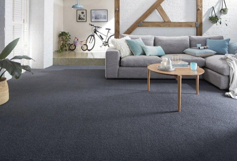 A living room carpeted in deep charcoal, a pale sofa and a round table on it.