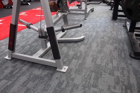 A gym floor in hard-wearing carpet tile beneath weight equipment.