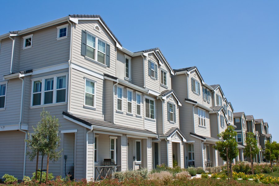 A row of grey clapboard townhouses on a landscaped street.