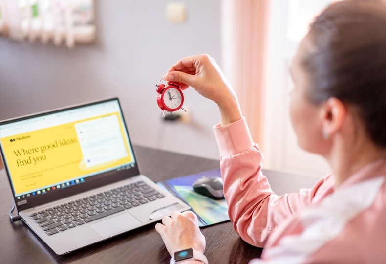 A woman at a laptop holding up a small red timer as she books a date.